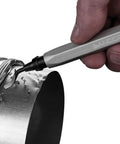 Badass Deburring Tool With Ten Spare Blades And Sharp Scribe stored in hand, smoothing rough edges on metal surface.