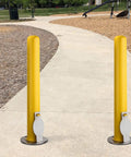 4X36 Inch Badass Removable Bollard With Embedment Sleeve Powder Coated Yellow Carbon Steel beside a paved walkway in a park