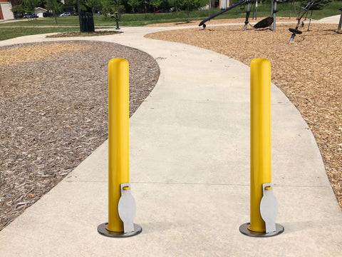 4X36 Inch Badass Removable Bollard With Embedment Sleeve Powder Coated Yellow Carbon Steel beside a paved walkway in a park