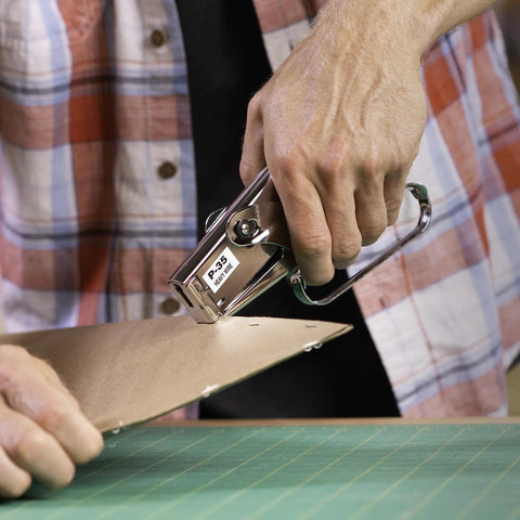 Person using Heavy Duty Handheld Plier Stapler Makes Stapling Paper Bags Thin Plastics Cardboard A Breeze With Its Tough Build And Comfortable Grip Handles Perfect For Office Shops Home Crafts And Insulation Jobs Using One Fourth And Three Eighth Inch Staples on cardboard