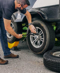 Man using Curved Trailer Aid With Wheel Chock And Rubber Base Pad, Six And A Half Inch Lift, Fits Trailers Up To Twenty Thousand Pounds And Tires Up To Thirty Two Inches, No Jack Needed For Easy RV And Camper Tire Changes Made In USA to change trailer tire