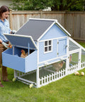 Woman standing next to a light blue Weatherproof Wooden Chicken Coop With Indoor Outdoor Walk In Hen House, Run, Nesting Box And Pull Out Tray