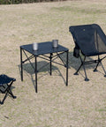 Ultra Lightweight Stable Folding Aluminum Table With Roll Up Top And Carry Bag For Camping Picnics Beach Chill Backyard Barbecues Tailgating And RV Trips Anywhere. Shown set up outdoors with camping chairs.