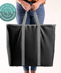 Person holding a black laundry tote with gray handles, highlighting its 100% recycled polyester fabric.