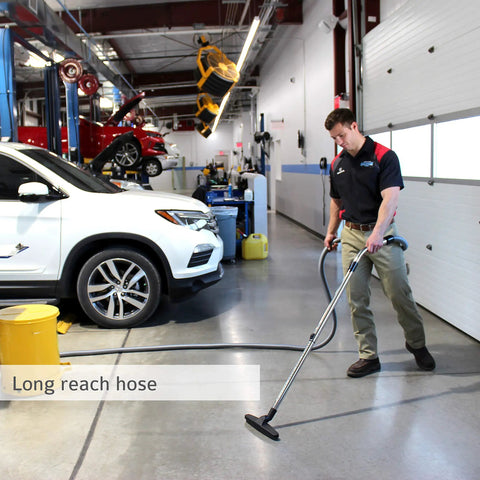 Man using Wall Mounted Garage Shop Vacuum Cleaner With 30 Ft Hose And 7 Gallon Bag in an auto shop to clean debris.
