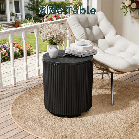 Black outdoor umbrella stand with fluted vertical ribbed design next to a patio chair, on round beige mat.