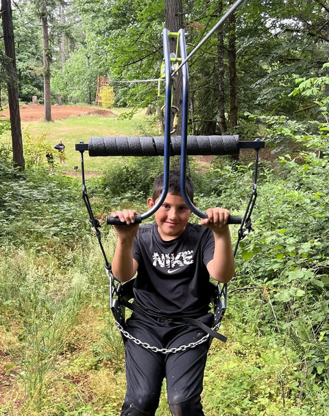Child using Backyard Zipline Seat For Trolley Use Heavy Duty Black Metal Swing Seat That Supports Up To 300 Lbs in forest