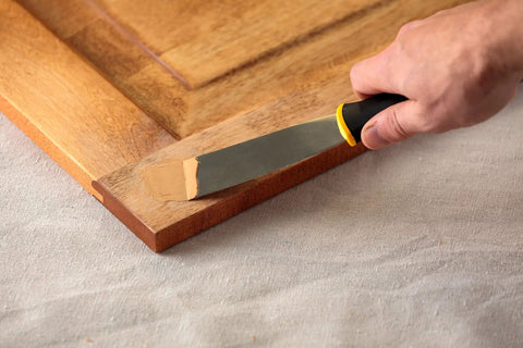 Applying Color Matched Wood Filler In Golden Oak No Sand Ready To Use 6 Oz with putty knife on wood surface corner
