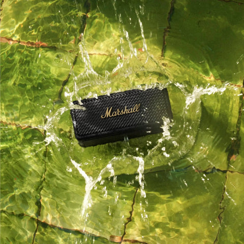 Emberton II Portable Bluetooth Speaker With 360 Degree True Stereophonic Sound, rugged black and brass in water splash.