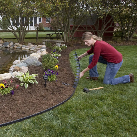 Person installing No Dig Landscape Edging Kit, 100 Ft Flexible Black Border With 32 Anchoring Spikes, around garden area.