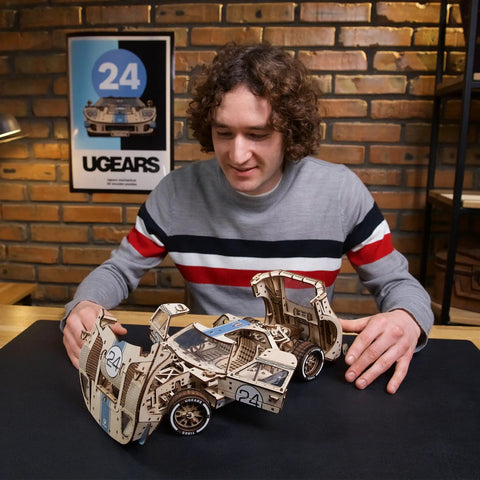 Man assembling Endurance Racer 3D Wooden Puzzle Kit for Adults, DIY Mechanical Car Model With Realistic Transmission, Pistons, Suspension, and Radiator Fan, Wood Sports Car Brain Teaser and Epic Hobby Gift on table