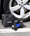 12V Portable Air Compressor Pump with Digital Tire Inflator beside car tire, cigarette lighter power visible