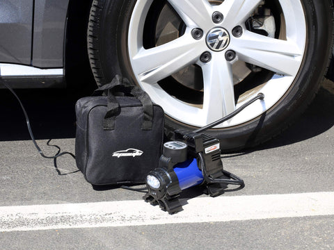 12V Portable Air Compressor Pump with Digital Tire Inflator beside car tire, cigarette lighter power visible