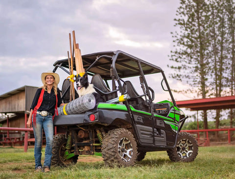 Woman with a dog and farm supplies on an ATV in a rural paddock setting.