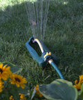 TurboTek 3200 Sq Ft Oscillating Sprinkler With 16 Rubber Nozzles QuickConnect Adapter watering lawn with sunflowers nearby
