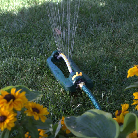 TurboTek 3200 Sq Ft Oscillating Sprinkler With 16 Rubber Nozzles QuickConnect Adapter watering lawn with sunflowers nearby