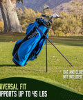 Workhorse Aluminum Golf Bag Stand Attachment With Slick Folding Legs That Anchors Your Cart Bag Firmly And Blocks Nasty Scratches While You Enjoy Smooth Playing Days Out On The Links Black holding a golf bag on green grass.