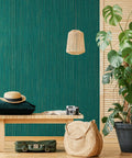 Interior with teal green grasscloth peel and stick wallpaper on wall, featuring a bench, plants, and a woven pendant light.