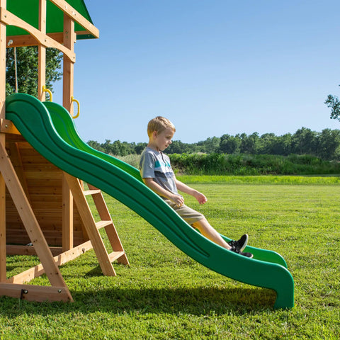 Child playing on wave slide of Cedar Wood Swing Set With Wave Slide And Elevated Play Deck, Double Rock Wall, Rope Ladder, Web Swing