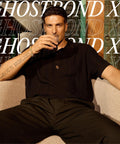 Man sitting with a drink, wearing dark clothing, in front of Ghostbond XL text background.