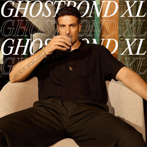 Man sitting with a drink, wearing dark clothing, in front of Ghostbond XL text background.
