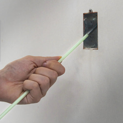 Hand using Glo Fish 15 Ft Glow In The Dark Fiberglass Fish Sticks Kit to insert rod into electrical box on wall.
