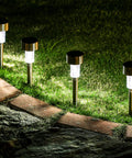 Four 16 Pack Solar Lights Outdoor Waterproof Stainless Steel LED Garden Lights line a brick pathway, illuminating grass at night.