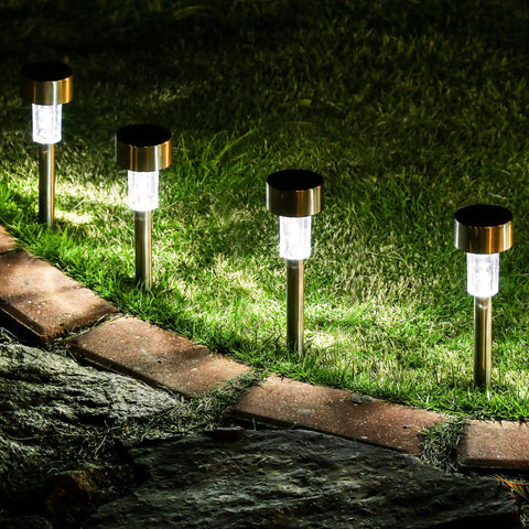 Four 16 Pack Solar Lights Outdoor Waterproof Stainless Steel LED Garden Lights line a brick pathway, illuminating grass at night.