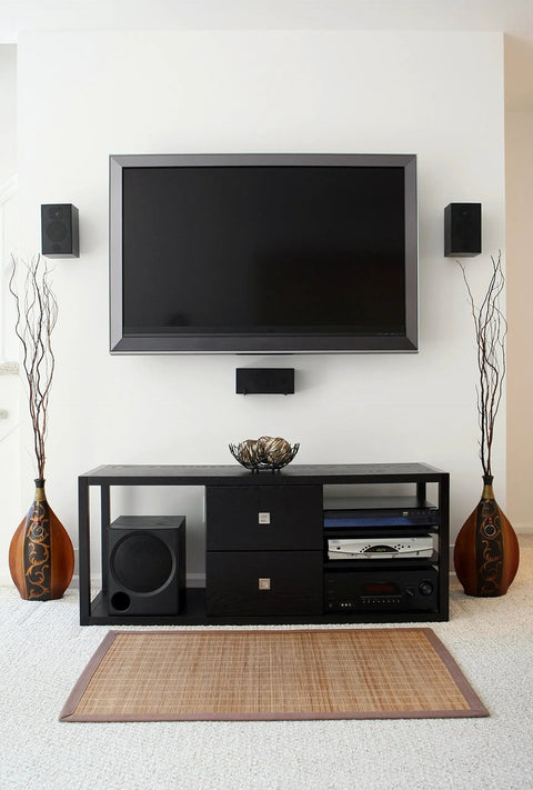 Modern living room setup with wall-mounted TV, sleek black media console, two tall vases, and stereo system beneath.