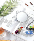 Double Sided Handheld Mirror With 1X And 2X Magnification Clear Handle Round Makeup Mirror For Face Detailing And Mascara Application Great For On The Go on a magazine with makeup items
