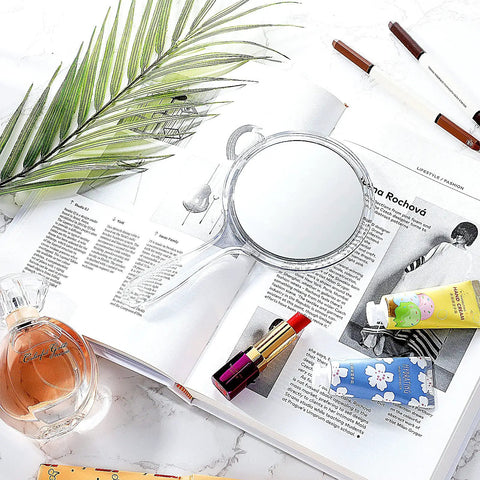 Double Sided Handheld Mirror With 1X And 2X Magnification Clear Handle Round Makeup Mirror For Face Detailing And Mascara Application Great For On The Go on a magazine with makeup items