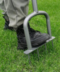 Person using Go-To Manual Lawn Aerator for compacted soil aeration, pushing foot bar into the ground with steel tines visible.