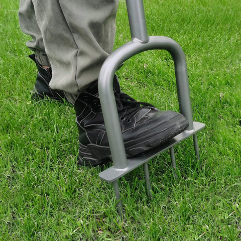 Person using Go-To Manual Lawn Aerator for compacted soil aeration, pushing foot bar into the ground with steel tines visible.