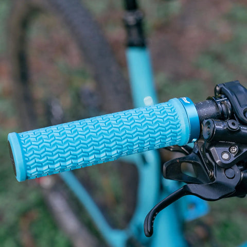 Close-up of blue lock-on mountain bike grip on handlebars, showing textured pattern and secure locking mechanism.