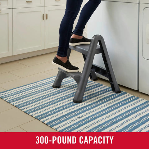 Two Step Folding Foot Stool 14 Inch High Gray Lightweight 300 Pound Capacity in use in a kitchen setting by an adult.
