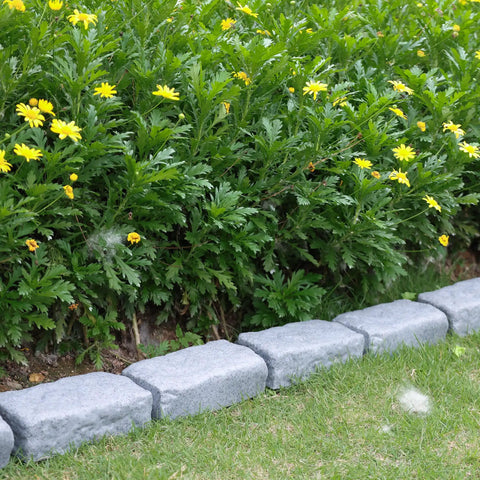 Realistic Faux Stone Landscape Edging Kit With 24 Bricks, 15.5 Ft Total, beside yellow flowers and green foliage in garden