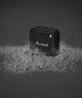 Willen II Portable Bluetooth Speaker With Rugged Waterproof And Dust Proof Design surrounded by dust, black and brass detail