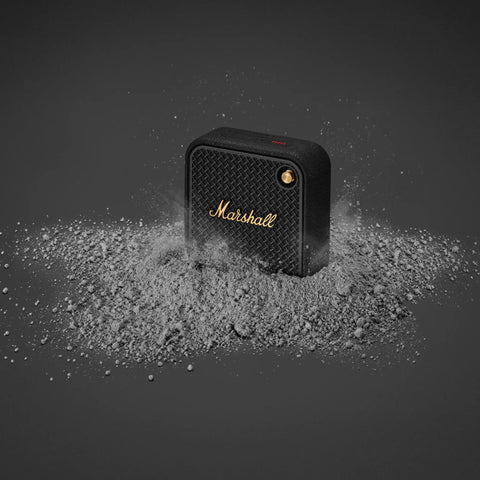 Willen II Portable Bluetooth Speaker With Rugged Waterproof And Dust Proof Design surrounded by dust, black and brass detail