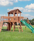 Cedar Wood Swing Set With Wave Slide And Raised Clubhouse Plus Balcony, Wooden Bridge, Rock Wall, Belt And Web Swings, Trapeze, Climbing Wall, Ladder And Outdoor Playset For Kids on green lawn.