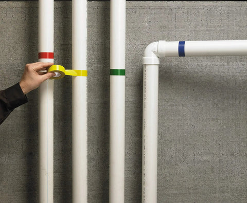 Person applying yellow tape on pipes with blue, red, and green marked, showcasing color separation use.