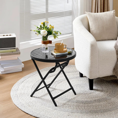 Outdoor Folding Round Patio End Table With Silk Tempered Glass Top And Lightweight Steel Frame beside a white armchair.