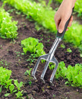 Side view of Mr. Pen black mini hand rake with metal 3-prong fork being used to turn soil among greens.