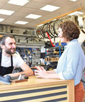 Bike shop employee assisting customer at a counter surrounded by bicycles and accessories in a well-lit store.
