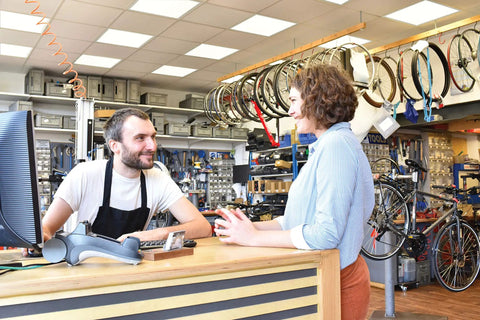 Bike shop employee assisting customer at a counter surrounded by bicycles and accessories in a well-lit store.
