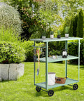 Flat Out Sturdy Three Tier Rolling Kitchen Cart Slick Green Metal Server With Tough Casters And Dual Hand Grips For Premium Indoor Coffee Tea Bar Display in garden with plants and tools.