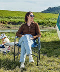 Woman sitting on Directors Chair For Outdoors With Side Table Foldable Camping Chair For Adults near a tent with scenic backdrop.