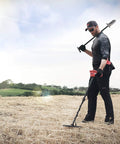 Minelab Vanquish 440 metal detector in use by an adult man outdoors in a dry field