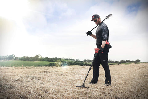 Minelab Vanquish 440 metal detector in use by an adult man outdoors in a dry field