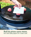 Hand placing patty paper on raw burger patties on grill from Smash Burger Kit With Cast Iron Press, Spatula, Seasoning Shaker And Patty Papers For Perfect Grillin At Barbecues And Tailgates, Mess Free Prep Every Time.