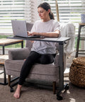 Person using Rolling Overbed Table With Wheels For Bedside, Sofa Or Recliner Adjustable Height Laptop Desk next to a chair.